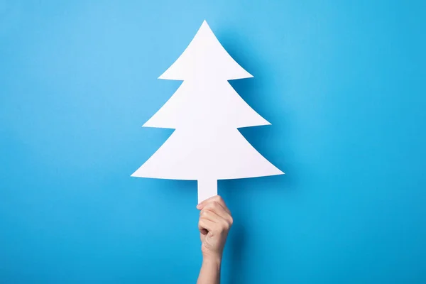 white christmas tree in hand over blue background, merry christmas concept