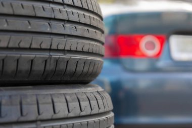 Bulanık mavi bir arabanın önüne yerleştirilmiş, otomatik servis veya ulaşım kavramları için uygun görünen, yatay kullanılmış lastik yığını..