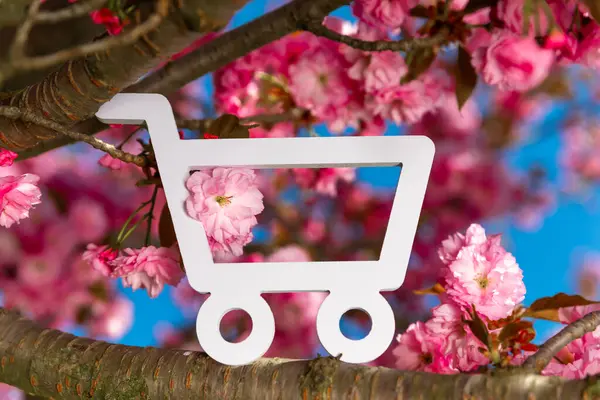 Beyaz alışveriş arabası sembolü, parlak pembe çiçekleri ve açık mavi gökyüzü ile çiçek açan kiraz ağacında sergilenir..