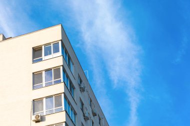 Beyaz cepheli ve açık mavi gökyüzünün altında geniş pencereli modern bir apartman dairesinin alçak açılı görüntüsü.