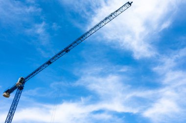 Uzun mavi kule vinci, aşağıdan bakıldığında dağınık bulutlarla dolu parlak bir gökyüzüne uzanıyor..