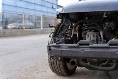 Hasarlı araç ön tamponu kayıp, motor parçaları ortaya çıkıyor, elektrik tesisatı ve çerçeve kentsel bir caddede..