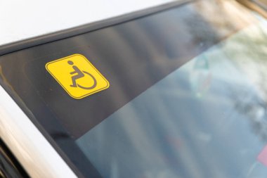 Bir arabanın camında sarı tekerlekli sandalye erişimi etiketi var. Engelli yolcu erişimine destek olduğunu gösteriyor..