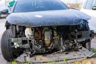 Tamponu eksik, karmaşık motor parçaları, turuncu kablolar ve iç parçaları olan hasarlı modern bir arabanın ön görüntüsü..