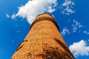 Yüksek, yuvarlak tuğla bir kule, görünür çatlaklar, canlı mavi bir gökyüzü karşısında dağınık bulutlar.