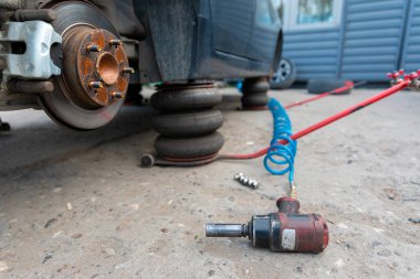 Araba hava krikosuyla kaldırılmış, fren merkezi açık, pnömatik ingiliz anahtarı ve yerde fındıklar var..