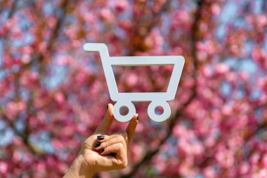 Elinde beyaz bir alışveriş arabası var. Güneşli bir günde hayat dolu pembe kiraz çiçekleriyle kesilmiş..