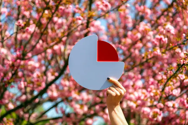 El ele tutuşan kırmızı ve beyaz pasta grafiği simgesi canlı bir çiçek açan pembe kiraz çiçeklerine karşı.