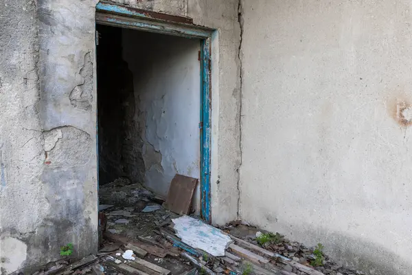 Çürüyen beton bir yapıda yıpranmış bir kapı aralığı. Boya soyulmuş, tuğla dökülmüş ve döküntülerle kaplı. İhmal edilmiş ve terk edilmiş..