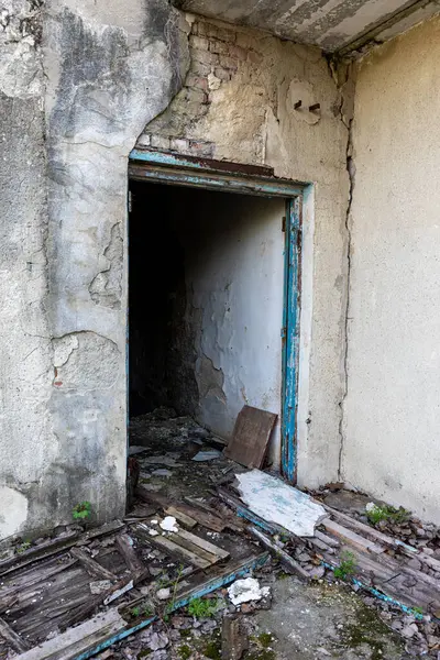 Çürümüş bir binanın girişi, kırık ahşap döküntüler, soyulmuş boyalar ve çatlak alçı duvarlar, ciddi ihmal belirtileri gösteriyor..