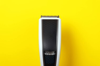 Canlı sarı bir arka planda modern bir elektrikli saç makasının yakın çekimi, bakım aletleri ve kişisel bakım ekipmanları sergileniyor.