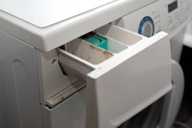 Açık bir çamaşır makinesi deterjan çekmecesinin yan görüntüsü. Kompartımanlarında görünür kir ve sabun birikintisi var..