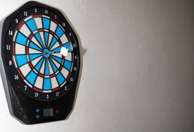 Duvara monte edilmiş elektronik dart tahtası, beyaz bir dart oku, açık renkli bir duvara karşı sergileniyor..