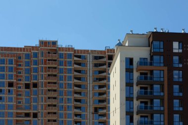 Modern, bitmiş bir apartmanın yan yana manzarası ve inşaat halindeki tuğla işçiliğine sahip bitişik bir bina..