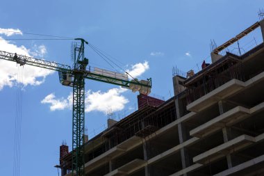 İnşaat halindeki beton binanın alçak açılı görüntüsü yeşil bir vinç ile bulutlu mavi bir gökyüzüne karşı..