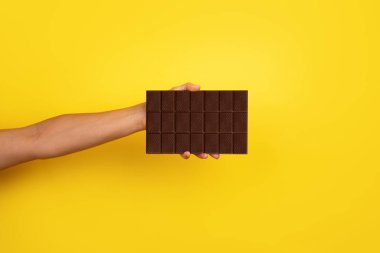 Genişletilmiş bir elin, parlak sarı bir arka plana karşı büyük siyah bir çikolata çubuğunu tutarken yakın plan görüntüsü..
