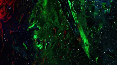 Su damlacıkları ve sıvı çizgileriyle dokunmuş canlı yeşil ve kırmızı neon yansımalı ıslak cam yüzeye yakın çekim.