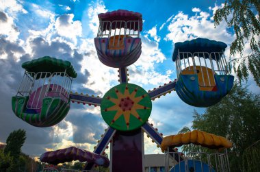 Dramatik bulutlu gökyüzüne karşı inşa edilmiş tuhaf kulübeleri olan canlı dönme dolap eğlence, eğlence ve çocukluk anıları için mükemmel bir tema..
