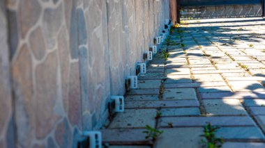 Güneşli tuğla bir patika boyunca taştan bir duvara bağlanmış beyaz plastik çit tokaları..