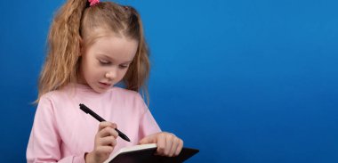 At kuyruklu genç bir kız kalemle deftere yazıyor, parlak mavi bir arkaplanda izole edilmiş, odaklanmış ve düşünceli bir ifade..