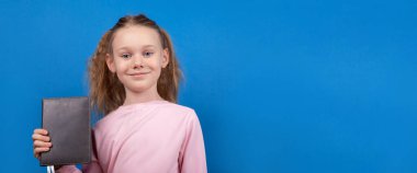 Pembe tişörtlü mutlu genç kız elinde parlak mavi bir arkaplan, metin veya kopya için boşluk tutuyor..