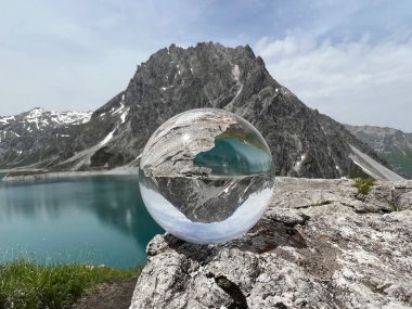 Arka planda, Avusturya 'nın en güzel dağlık göllerinden birini (Lnersee) yansıtan kristal küre Rtikon (Vorarlberg) bulunur.).