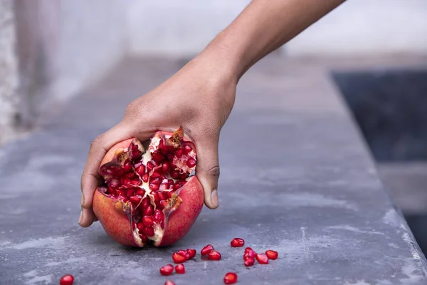 Ripe pomegranate fruit in woman hand on concrete background