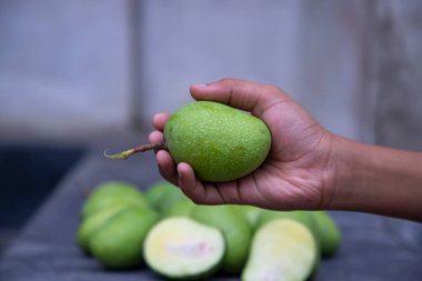 Bulanık arkaplanı olan el ele tutuşan çiğ yeşil mango.