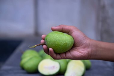 Bulanık arkaplanı olan el ele tutuşan çiğ yeşil mango.