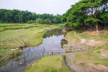 Nehir suyu, mavi gökyüzünün altındaki yeşillik manzarasıyla kanalın içinden akar.