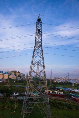 Şehir manzarası ve mavi gökyüzü arka planına sahip yüksek voltajlı elektrik direği.