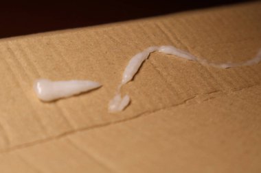 Kalın bir beyaz krem tabakası kaba karton yüzey boyunca cömertçe yayılarak çarpıcı bir karşıtlık yaratır.