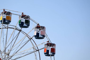 Parlak bir lunapark treni, açık mavi gökyüzüne karşı kurulmuş ve görünürde hiç insan yok.