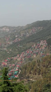 Himachal Pradesh 'teki çarpıcı bir tepe istasyonu manzarası, yemyeşil yapraklar, renkli evler ve görkemli dağlarla