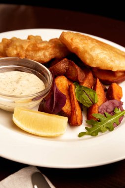 Bir tabakta haşlanmış balık ve pubda tahta bir masada patates kızartması. Sağlıksız yiyecekler