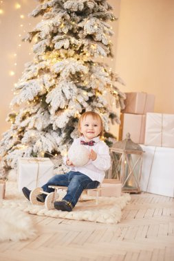 Gülümseyen çocuk Noel ağacının yanında duruyor. Mutlu yıllar ve mutlu Noeller..