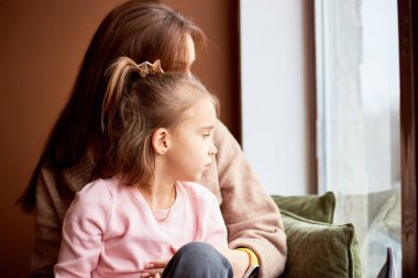 Little caucasian girl with mother looking at window and dreaming. A lot of gift boxes around. Happy family christmas concept