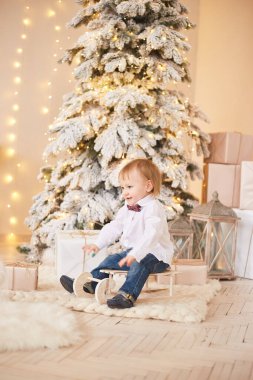 Gülümseyen çocuk Noel ağacının yanında duruyor. Mutlu yıllar ve mutlu Noeller..