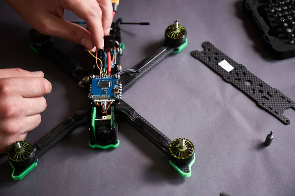 stock image Close up of man's hands assembling a drone from parts, using tools, Preparing high speed racing quadcopter for flight. Repair drone before training process.