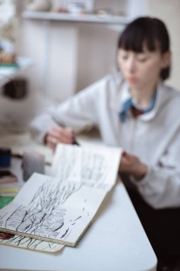 Kadın ressam çizimlerine kalem ve siyah mürekkeple bakıyor. Grafik boyama. Modern sanat yaratılıyor
