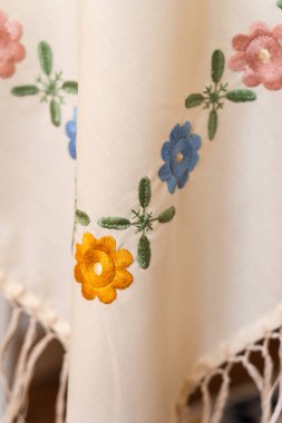 Karmaşık işlemeli beyaz kumaşın renkli çiçekler ve yapraklarla yakın plan görüntüsü..