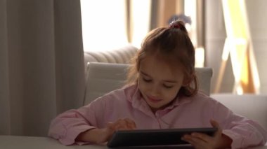 Tablet kullanan mutlu kız. Yoğun bir şekilde bir alete odaklanmış. Beyaz liseli kız Parlak Oturma Odasında Gün Boyunca Tabletle Nişanlı