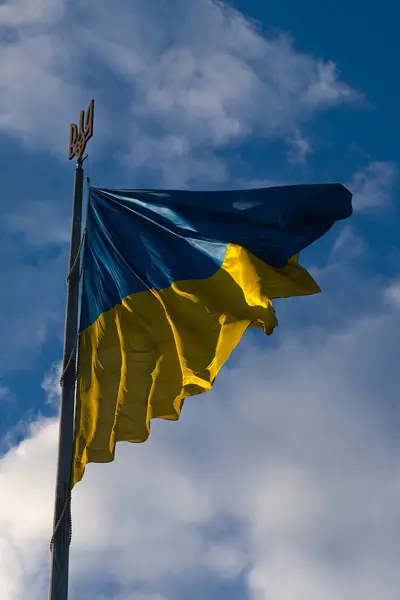 stock image Ukrainian flag waving under a cloudy sky at a public location, symbolizing national pride and unity on a bright day