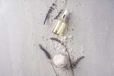 Lavanta yağı, banyo tuzu ve kurumuş çiçeklerle sükunet ve rahatlama ayini sırasında açık gri bir arka planda.