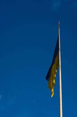 Ukrayna bayrağı bulutlu bir gökyüzünün altında halka açık bir yerde sallanıyor, parlak bir günde milli gurur ve birliği simgeliyor.