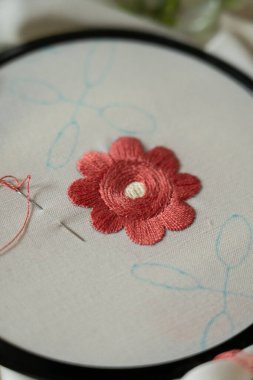El yapımı karmaşık bir nakış, pembe bir çiçeğin bir halkanın içinde, el yapımı bir masa üzerinde.