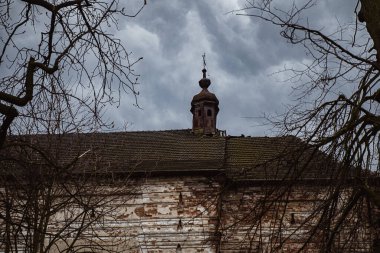 Kırsal alanda bulutlu bir gökyüzünün altında çıplak ağaçlarla çevrili eski kilise kulesi. Tarihi kilise Yavoriv, Ukrayna