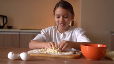 Çocuk basit malzemelerle pişirme becerilerini öğrenirken rahat bir mutfakta hamurdan zevk alıyor.