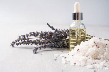 Lavanta banyosu ürünleri ve aksesuarlar serpilmiş tuz ve bitki filizi ile hafif bir arka planda düzenlenmiştir.