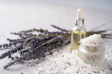 Lavanta banyosu ürünleri ve aksesuarlar serpilmiş tuz ve bitki filizi ile hafif bir arka planda düzenlenmiştir.